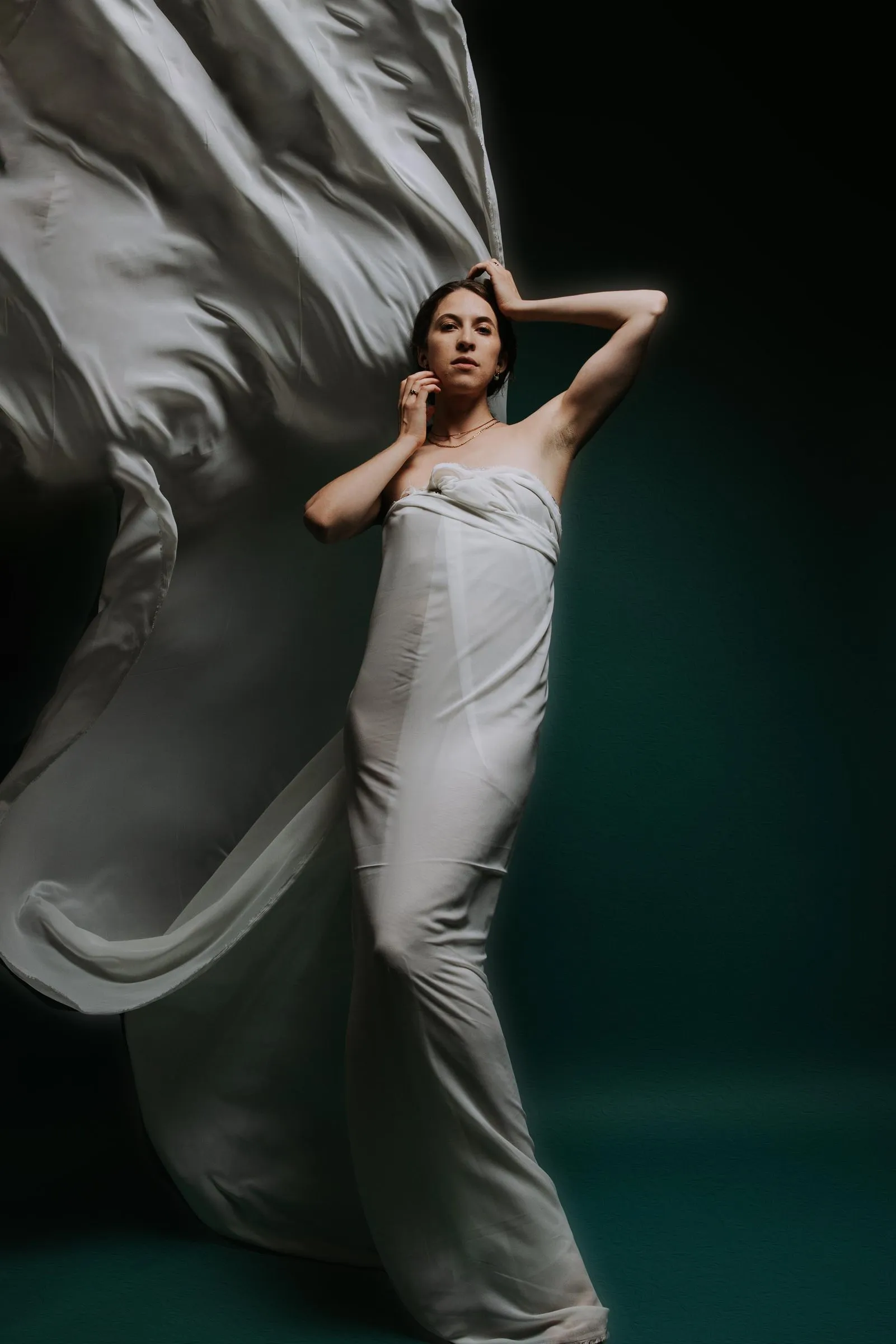 Alex Schooling with a long train of white silk against teal