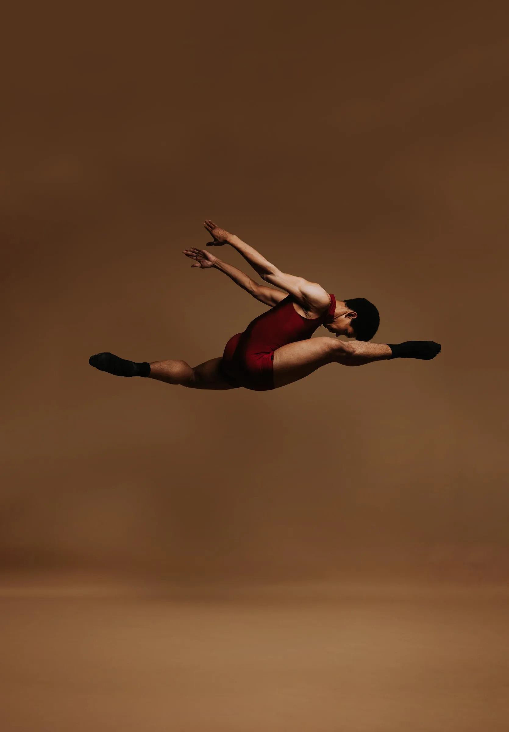 A dancer in a burgundy leotard mid-leap