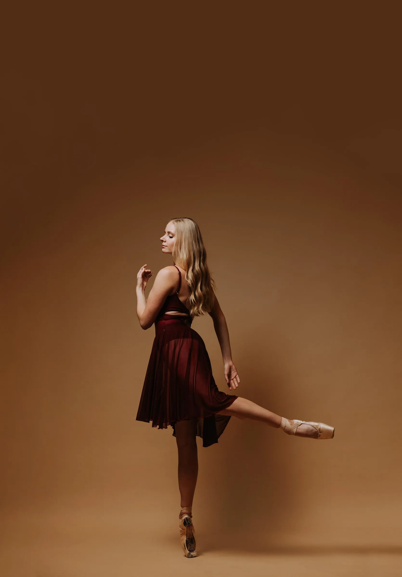 A dancer in a burgundy dress extending one leg on pointe