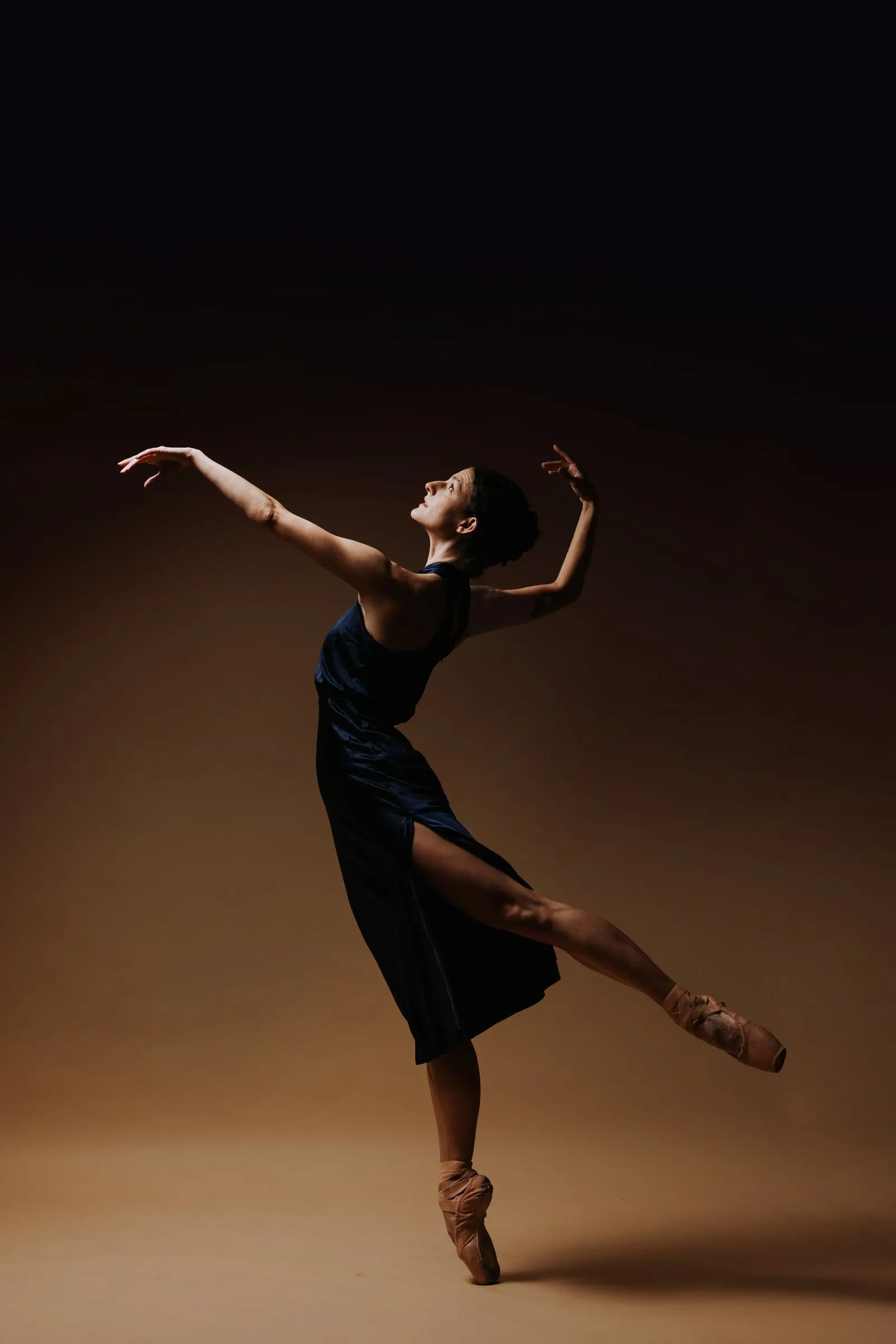 Grace Manuel in a navy dress, mid-step on pointe