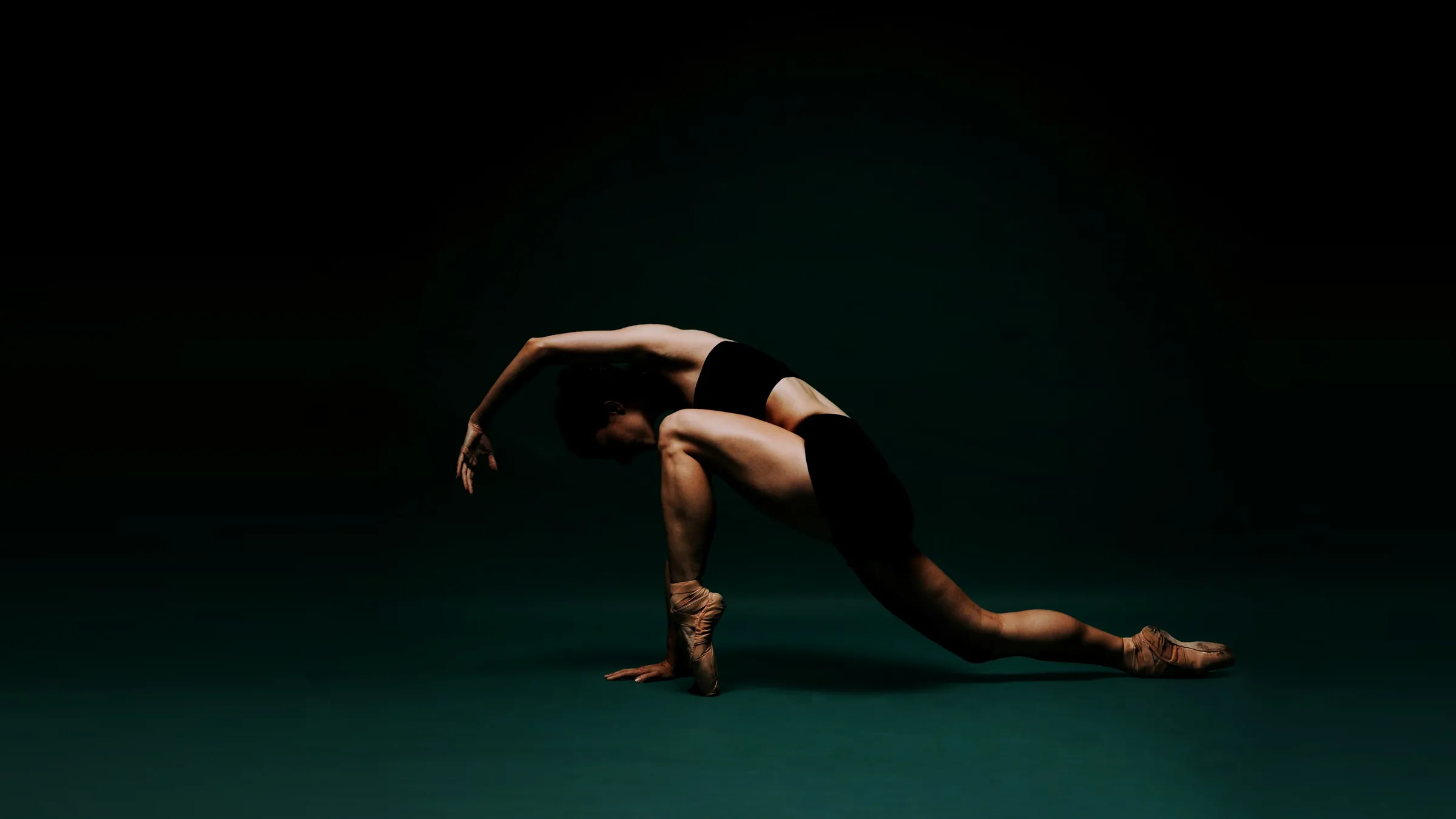 Grace Manuel in a deep, arched lunge on a dark teal stage